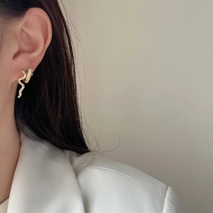 Elegant gold-plated snake earrings with white zircons and green gemstone eyes on model