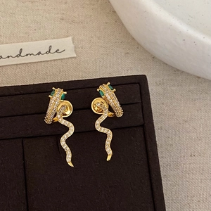 Close-up of gold snake stud earrings with pavé white zircons and green gemstone eyes