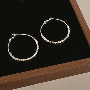 Close-up of silver hoop earrings featuring faceted metal beads on a black display tray