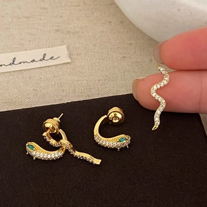 Golden snake earrings with white crystals and green stone eyes in a minimalist style