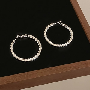Macro shot of silver twisted hoop earrings with a metallic finish on a black mirror surface