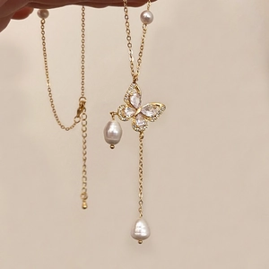 Detail of a gold butterfly pendant with rhinestones and white freshwater pearl drop