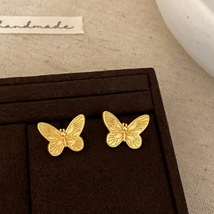 Close-up of golden butterfly stud earrings with pearl tassel on a dark velvet display