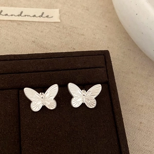Macro shot of silver butterfly stud earrings with fine texture on a velvet jewelry box