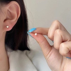 Minimalist small white heart stud earrings with gold plating shown on ear and in hand