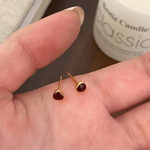 Close-up of elegant gold stud earrings with tear-drop ruby stones held by hand