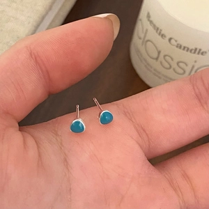 Close-up of mini triangle stud earrings with turquoise stones held in a palm
