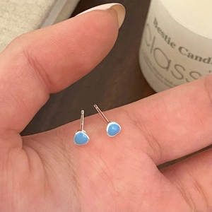 Close-up of minimalist blue enamel stud earrings held by hand to show micro size