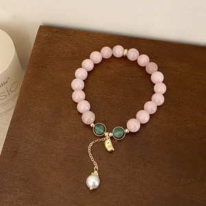 Bracelet en pierres naturelles roses avec touches vertes et breloque perle sur fond de bois