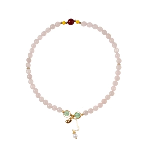 Détail du bracelet en perles de pierre rose avec disque vert, cœur doré et pendentif perle