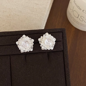 Close-up of floral silver earrings with brushed petals and clear center zircon