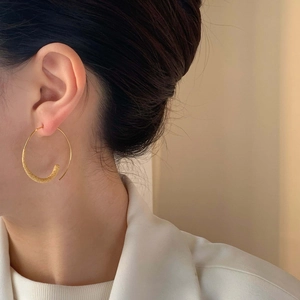 Élégantes boucles d'oreilles créoles dorées avec texture mate sur un mannequin