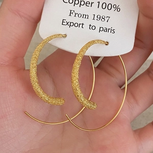 Détail macro de créoles en cuivre doré montrant des textures mates et polies raffinées