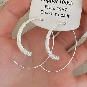 Détail macro de grandes créoles en cuivre argenté avec une surface à texture mate