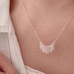 Minimalist silver tassel necklace featuring a fan-shaped fringe pendant on a lace blouse
