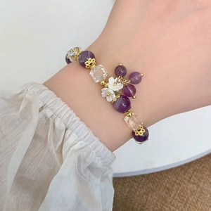 Minimalist purple crystal bracelet with flower pendant on model wrist against cozy texture