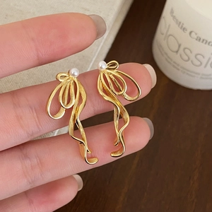 Detail of elegant gold ribbon earrings with white pearls held against a cozy candle