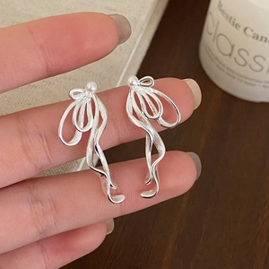 Close-up of bow-shaped ribbon earrings with a white pearl held on fingers