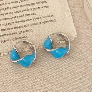 Close-up of twisted silver-tone earrings featuring glossy sky blue enamel on linen background