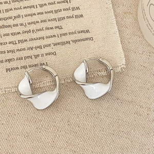 Macro shot of silver mobius hoop earrings with white enamel on vintage linen fabric