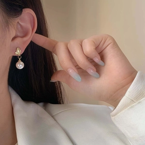 Elegant gold leaf earrings with white round pearl pendants shown on model