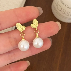 Close-up of elegant pearl drop earrings with heart-shaped golden leaf design details