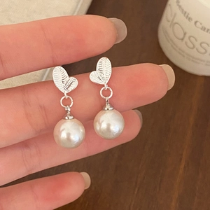 Detail view of silver leaf pearl earrings held by hand against a warm background