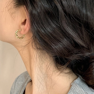 Detail of C-shaped gold hoop earrings with grainy texture worn by a model on side profile