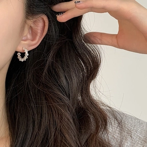 Close-up of C-shaped silver earrings with sparkling crystals worn on ear for detail