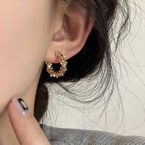 Detailed close-up of a gold textured C-shape earring worn by a model in a minimal setting