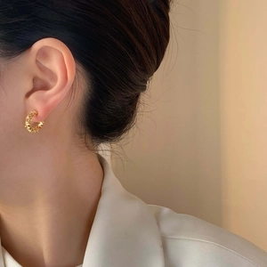 Close-up of gold C-shaped textured earrings with wrinkled artistic design on model