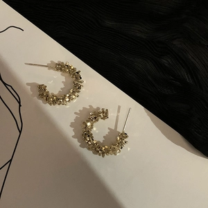 Macro detail of gold C-shaped earrings featuring a textured crushed silver lava effect