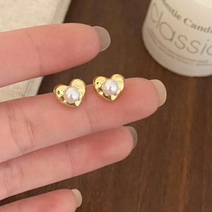 Elegant heart-shaped gold stud earrings with white pearl detail held in hand