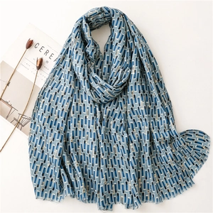 Lightweight blue geometric scarf with gold foil accents and fringe, styled on a magazine