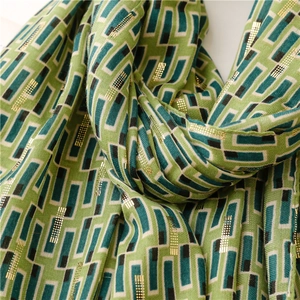 Macro detail of green scarf showing golden foil geometric prints and soft woven texture