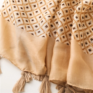 Détail des motifs géométriques et des pompons sur une écharpe en coton jaune