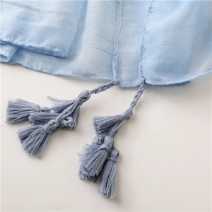 Macro shot of light blue cotton linen scarf featuring intricate tassel hem and woven texture