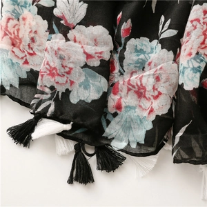 Close-up of bohemian floral scarf with pink roses, black fabric, and fine fringe details
