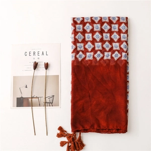 Écharpe rouge brique aux motifs floraux bleus et franges sur un fond minimaliste épuré