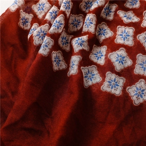 Détail macro de l'écharpe bordeaux avec des motifs floraux géométriques bleus et blancs
