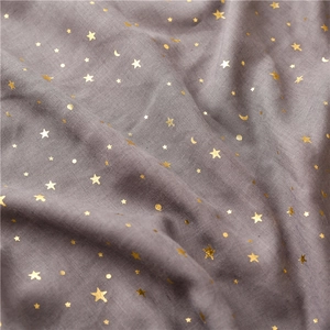 Detail shot of soft grey fabric with gold foil star and moon pattern and fringe trim