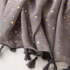 Detail of gray scarf with gold foil star and moon patterns and fringed tassels
