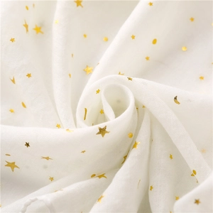 Macro detail of soft white scarf featuring golden foil star and moon patterns with tassels