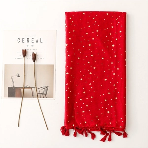 Detail of red scarf with gold star moon patterns and fringe tassels on a white surface