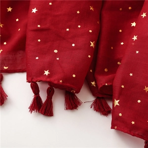Detail of dark red cotton feel scarf with gold star foil prints and delicate tassels