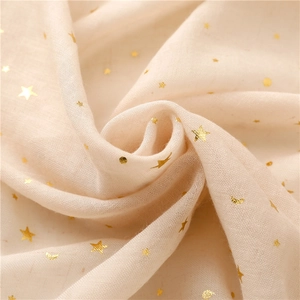 Macro detail of soft cream scarf featuring gold foil star and moon patterns with tassels