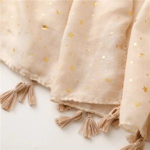 Detailed macro view of beige scarf featuring golden star moon patterns and fringe