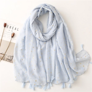 Light blue scarf with gold star prints and fringe tassels on a clean flat lay background