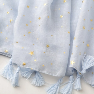 Detail of light blue shawl with gold foil stars, moons and tassel trim texture
