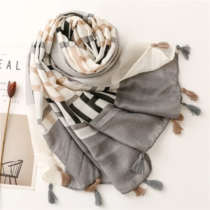 Detail of grey and beige geometric silk scarf with decorative tassels on white surface